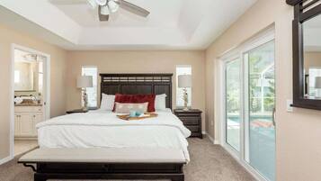 A bedroom with a large bed, a ceiling fan, a nightstand, a lamp, a bench, and a sliding glass door to the outside.