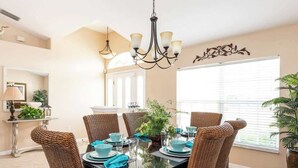 Une salle à manger avec une table en verre, des chaises en osier, de la vaisselle couleur turquoise et un lustre.