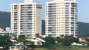 Two high-rise buildings with a beach and mountains in the background. - Velutti Pérola do Mar - Penha - SC (Penha)