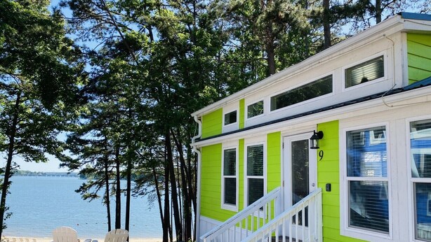 Una cabaña verde brillante con detalles blancos, una escalera y vistas a un lago.