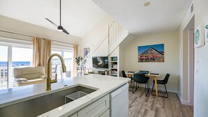 A modern kitchen with a large island, a dining area with a table and chairs, and a view of the city through large windows. - 30-A Loft with Gulf Views (Santa Rosa Beach)