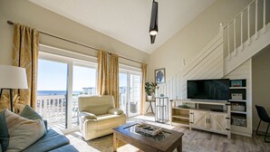 A spacious living room with a sofa, a coffee table, and a TV on a wooden stand. - 30-A Loft with Gulf Views (Santa Rosa Beach)