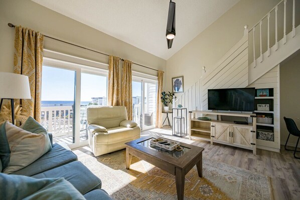 A spacious living room with a sofa, a coffee table, and a TV on a wooden stand. - 30-A Loft with Gulf Views (Santa Rosa Beach)