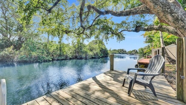 Une terrasse en bois avec une chaise donnant sur une étendue d’eau calme, le tout entouré d’une végétation luxuriante.