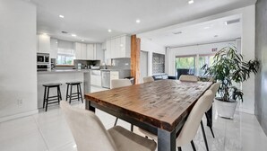 Une cuisine moderne avec des meubles blancs, une table à manger en bois et une plante en pot.
