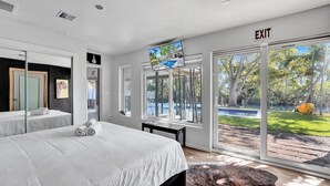 Une chambre d’hôtel moderne dotée d’un grand lit, d’une télévision, d’un bureau et offrant une vue sur une piscine et un jardin.