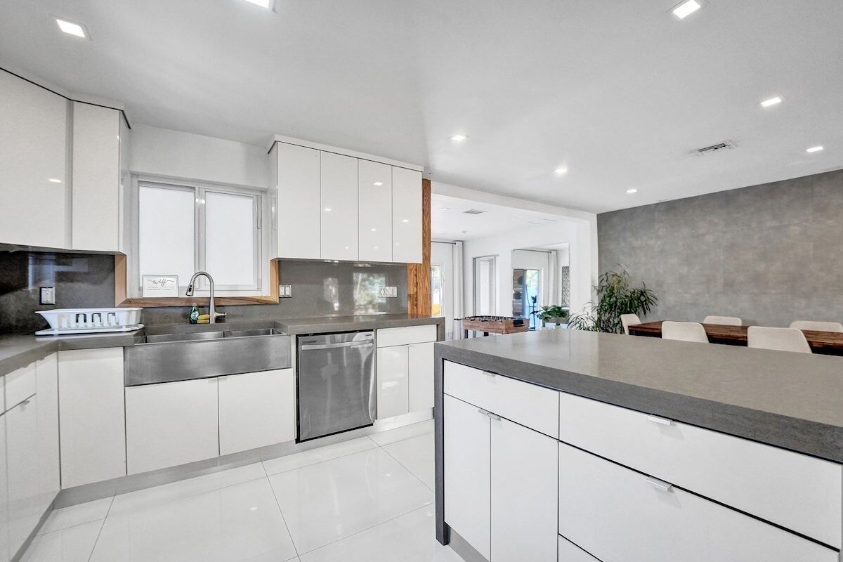 A modern kitchen with white cabinetry, a built-in dishwasher, and a large island with a grey countertop.