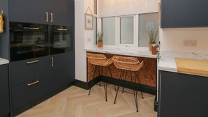 Una cocina moderna con armarios oscuros, horno empotrado, encimera de mármol y ventana con persianas.