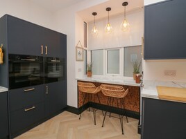 A modern kitchen with dark cabinetry, a built-in oven, a marble countertop, and a window with blinds.
