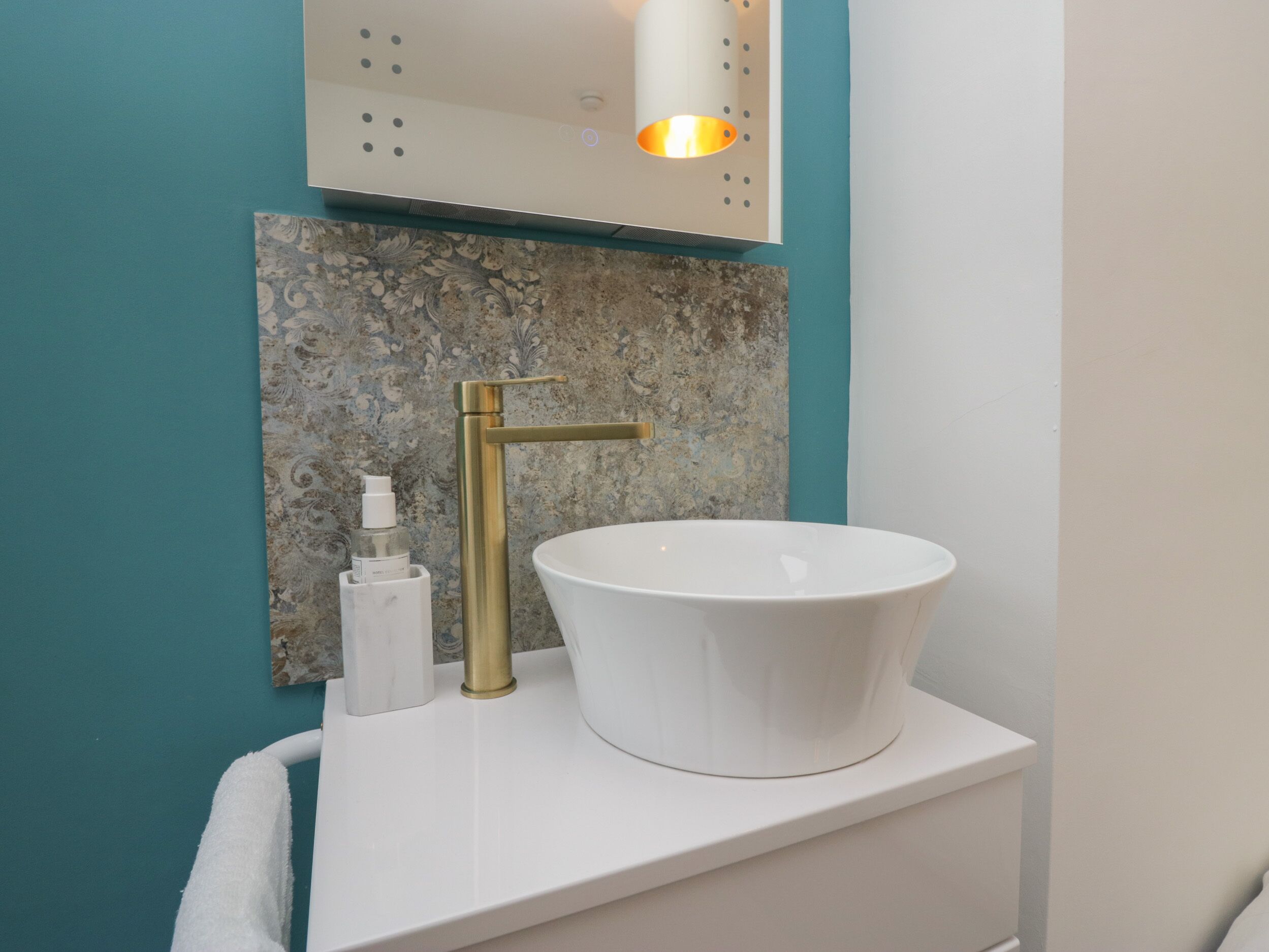 A bathroom with a white sink, gold faucet, and a mirror above it.