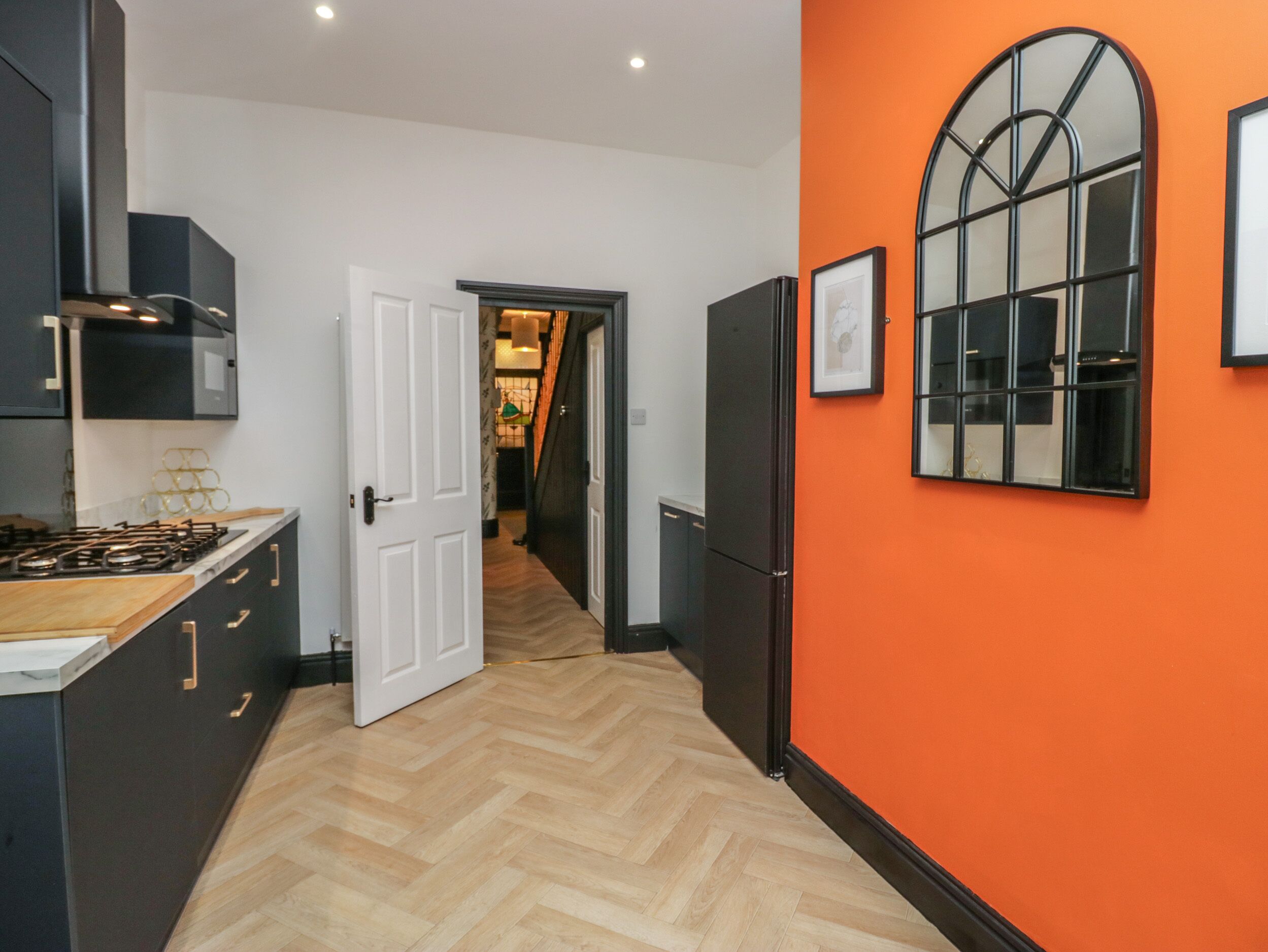 A modern kitchen with a herringbone floor, a large window, and a door leading to a hallway.