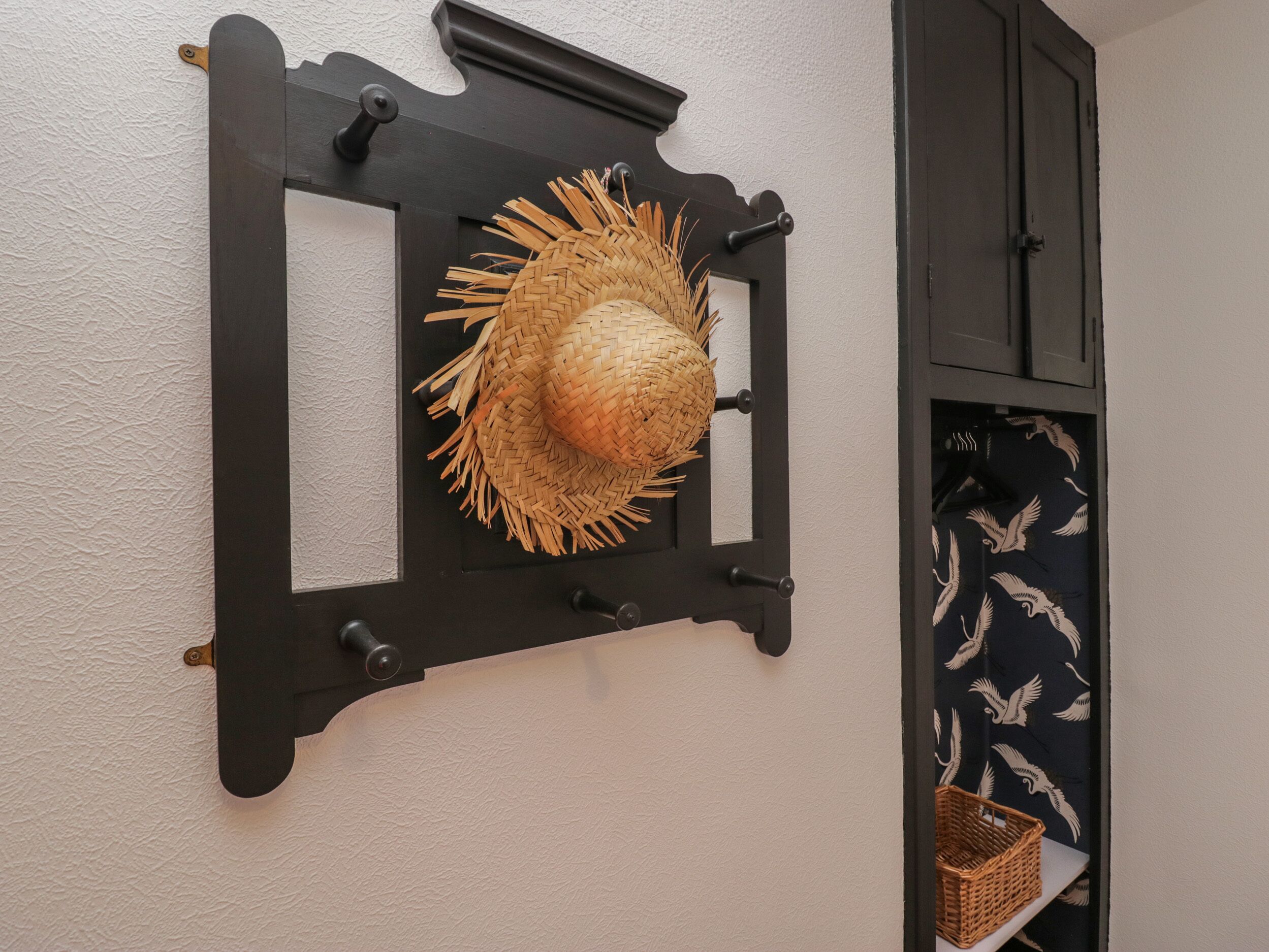A wall-mounted hat rack with a woven straw hat.