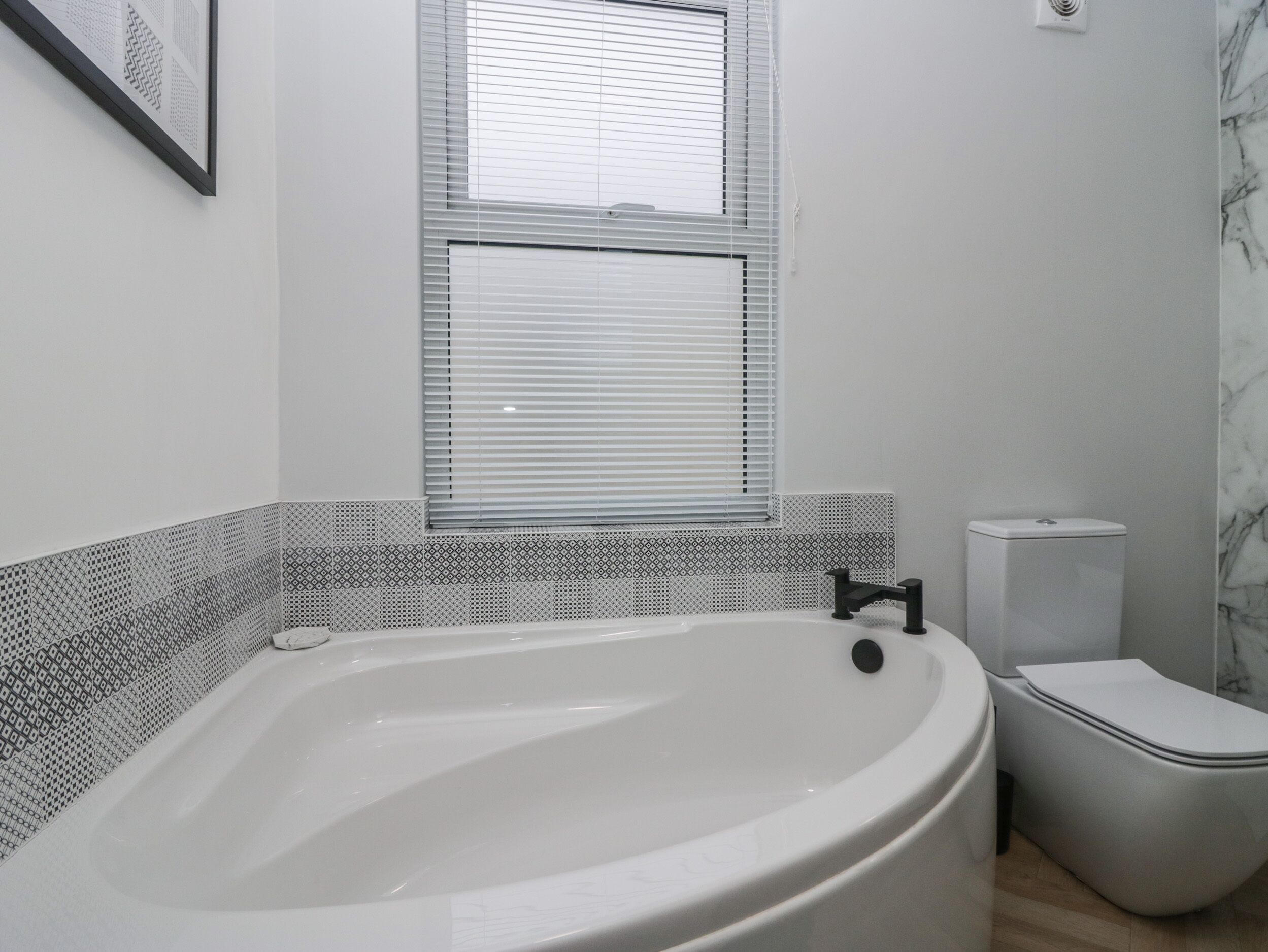 A bathroom with a freestanding bathtub, a toilet, and a window with blinds.