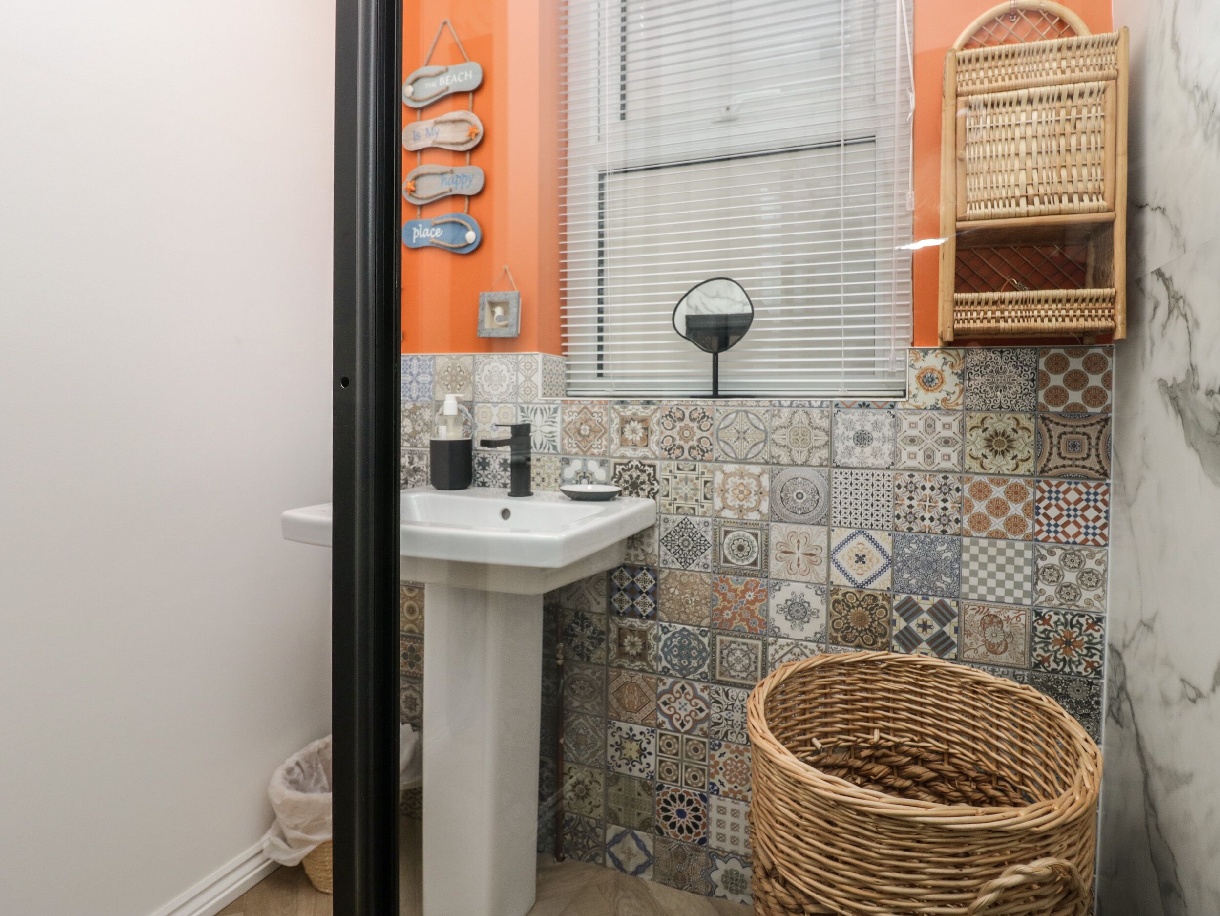 A bathroom with a white sink, decorative tiles, a wicker basket, and a wall-mounted mirror.