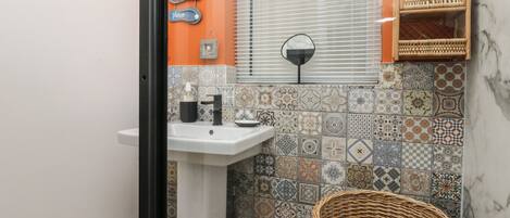 A bathroom with a white sink, decorative tiles, a wicker basket, and a wall-mounted mirror.