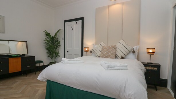 Un dormitorio ordenado con una cama grande, mesitas de noche, un espejo y una planta en maceta.