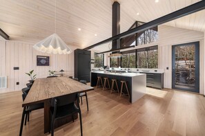 Enjoy meals in the spacious kitchen and dining area with a large island, wooden table, and pendant light.