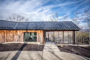 Un bâtiment moderne doté d’un toit métallique incliné, d’un revêtement en bois et d’un chemin en béton menant à une entrée avec une porte en verre.