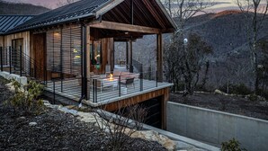 A modern cabin with a wooden exterior, a covered deck, and a view of the surrounding mountains.