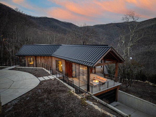 Une cabane moderne dotée d’une grande terrasse, d’une cheminée et d’un garage.