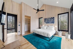 Une chambre à coucher moderne, dotée d’un grand lit, d’un ventilateur de plafond et offrant une vue sur l’extérieur grâce à de grandes fenêtres.