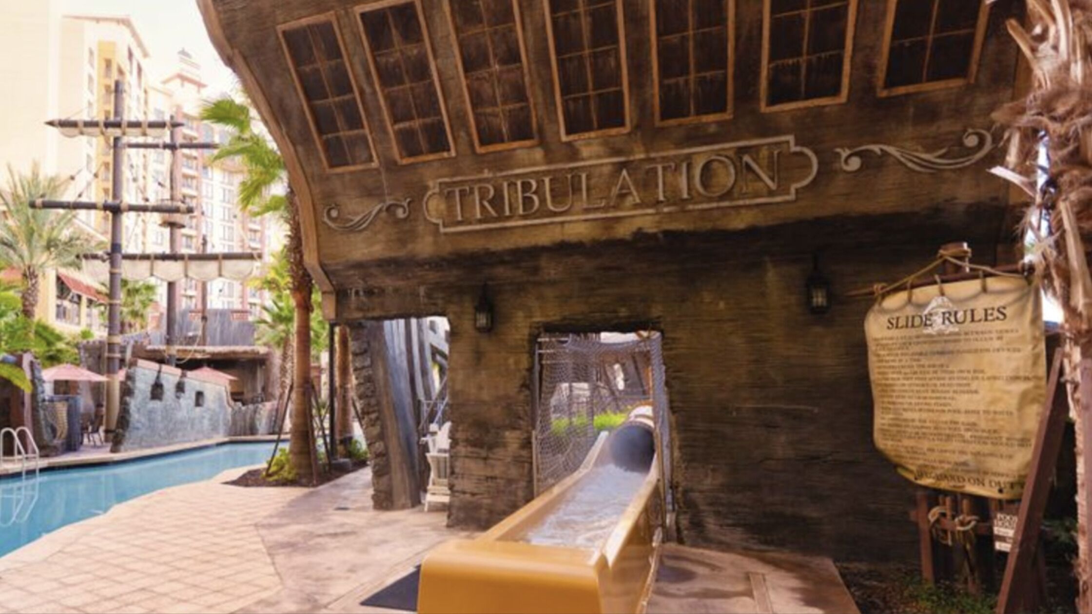 Une structure en bois sur laquelle est gravé le mot « TRIBULATION », un toboggan et un panneau indiquant « RÈGLES DU TOBOGGAN ».