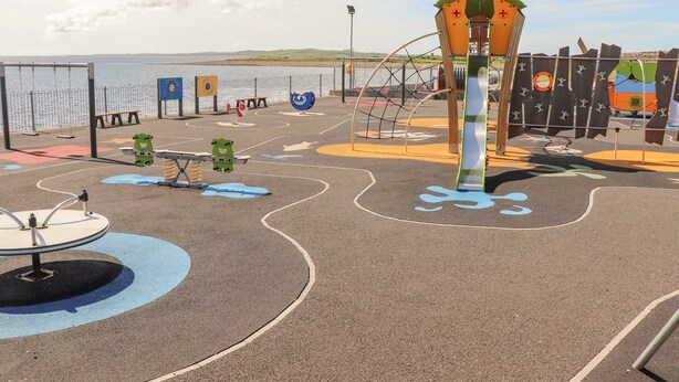 A playground with various play structures, including a slide and swings, near a body of water. - Cloughoge House (Kilrush)