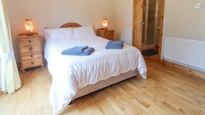 A bedroom with a wooden bed, two bedside tables with lamps, a wooden wardrobe, and a glass door leading to a bathroom. - Cloughoge House (Kilrush)