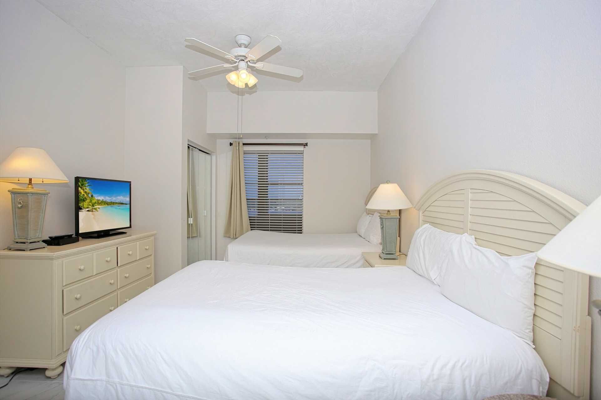 Une chambre d’hôtel avec un lit, une télévision, un ventilateur de plafond et une fenêtre avec des stores.