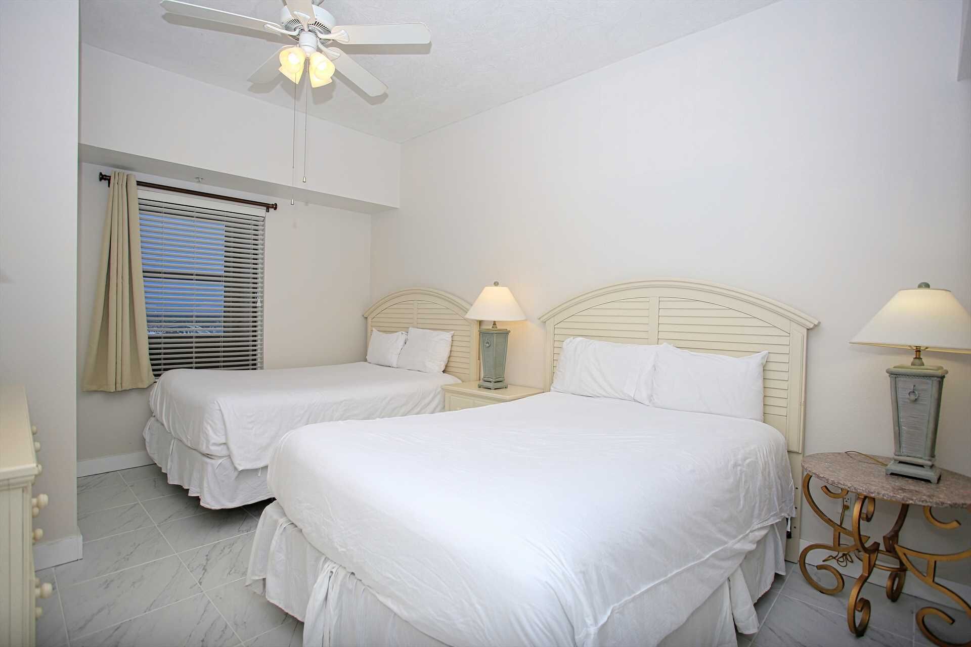 Une chambre d’hôtel avec deux lits, un ventilateur de plafond, une fenêtre avec des stores et une petite table avec une lampe.