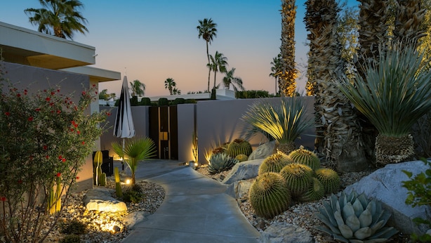 A well-maintained garden with a variety of cacti and succulents, a paved pathway, and a modern building in the background. - NEW! Private Pool & Mountain Views! (Palm Springs)