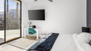 A bedroom with a bed, a desk, a chair, a TV, and a balcony with a view of mountains. - NEW! Private Pool & Mountain Views! (Palm Springs)