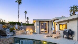 A modern outdoor pool area with a built-in barbecue, lounge chairs, and a well-lit patio. - NEW! Private Pool & Mountain Views! (Palm Springs)