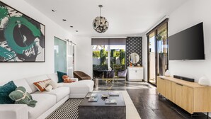A modern living room with a white sofa, a coffee table, and a TV on a wooden cabinet. - NEW! Private Pool & Mountain Views! (Palm Springs)