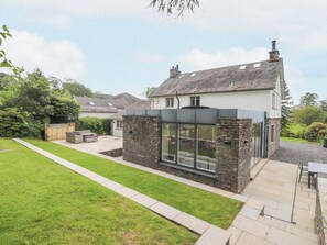 A modern house with a stone exterior, a large glass window, and a well-maintained lawn. - Grassings (Ambleside)