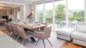 Un comedor espacioso con una gran mesa dispuesta para seis personas, un telescopio sobre trípode y vistas a un jardín exuberante a través de amplias puertas correderas.