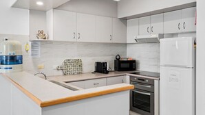 Una cocina moderna con gabinetes blancos, horno empotrado, microondas y cafetera.