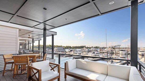 Un espacio de estar al aire libre cubierto con mobiliario de madera y vistas al puerto deportivo.