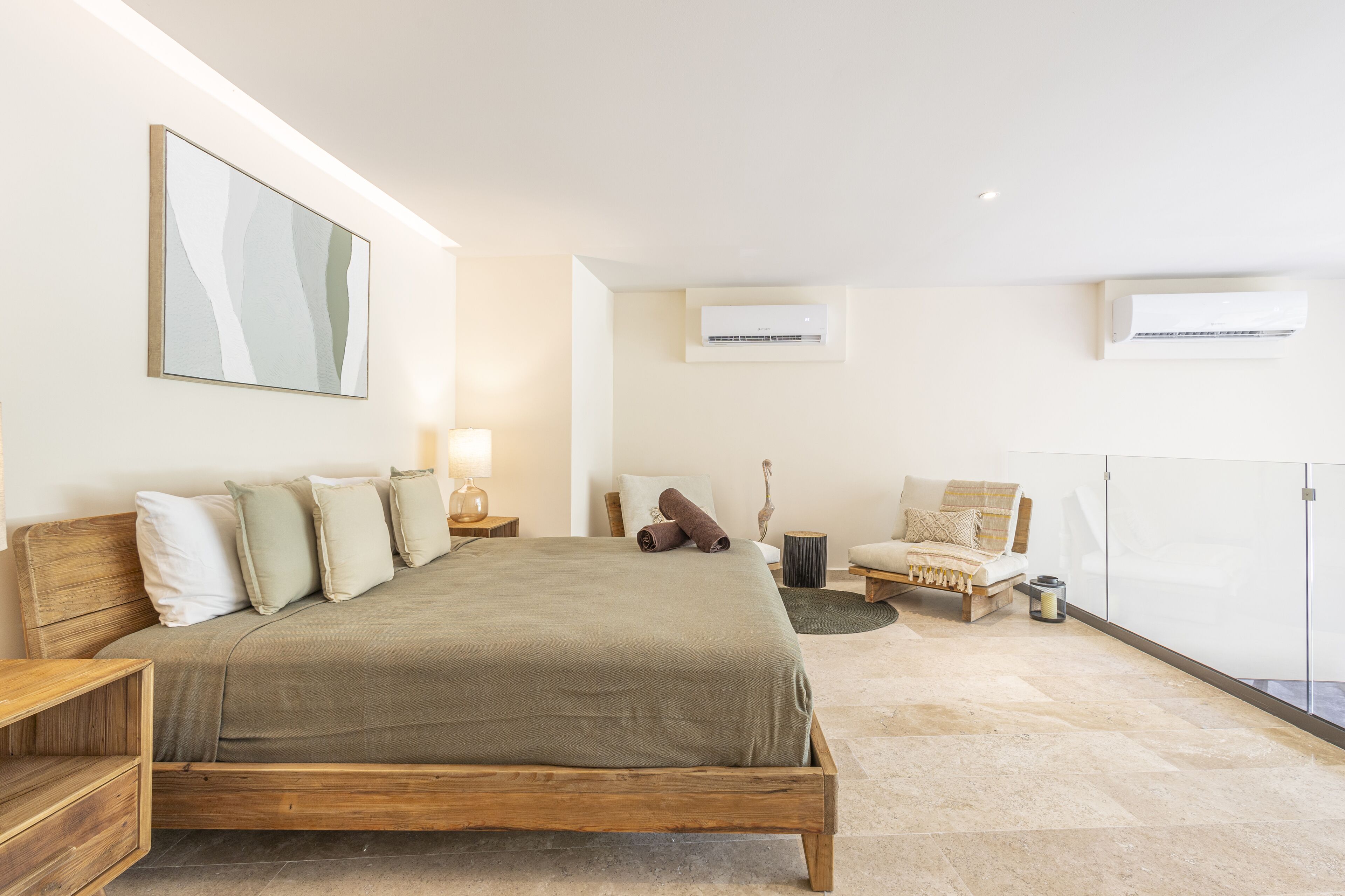 A bedroom with a large bed, bedside tables, a chair, a lamp, and an air conditioning unit.