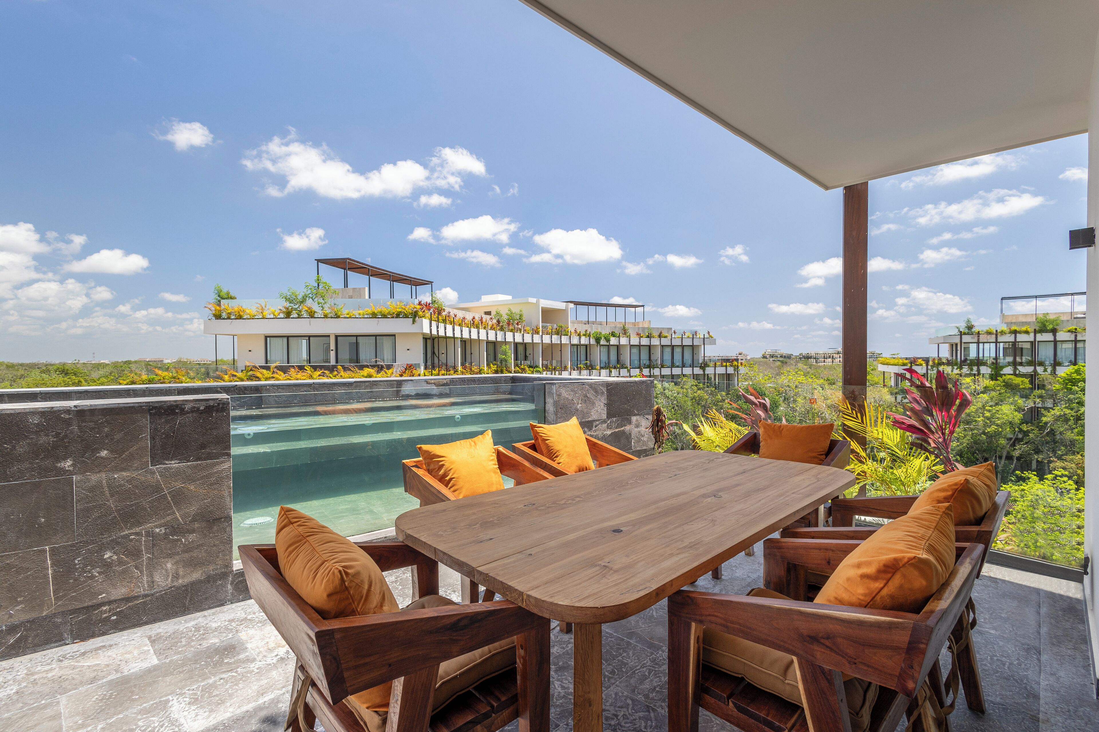 A modern outdoor dining area with a pool, wooden furniture, and a view of a residential complex.
