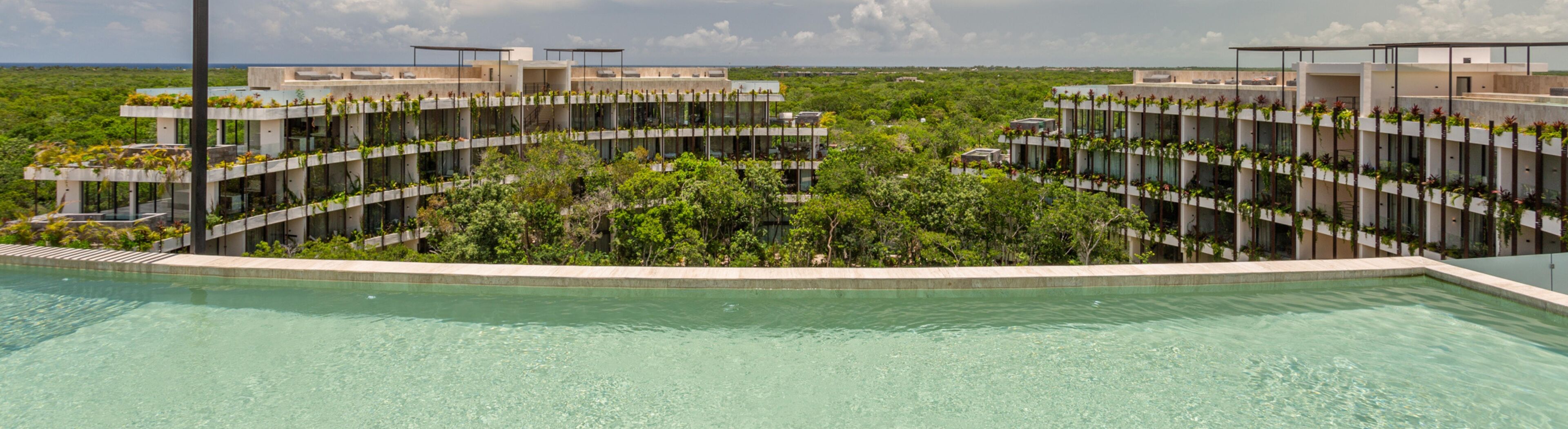 A modern resort with a central pool, surrounded by multi-story buildings with balconies adorned with plants.