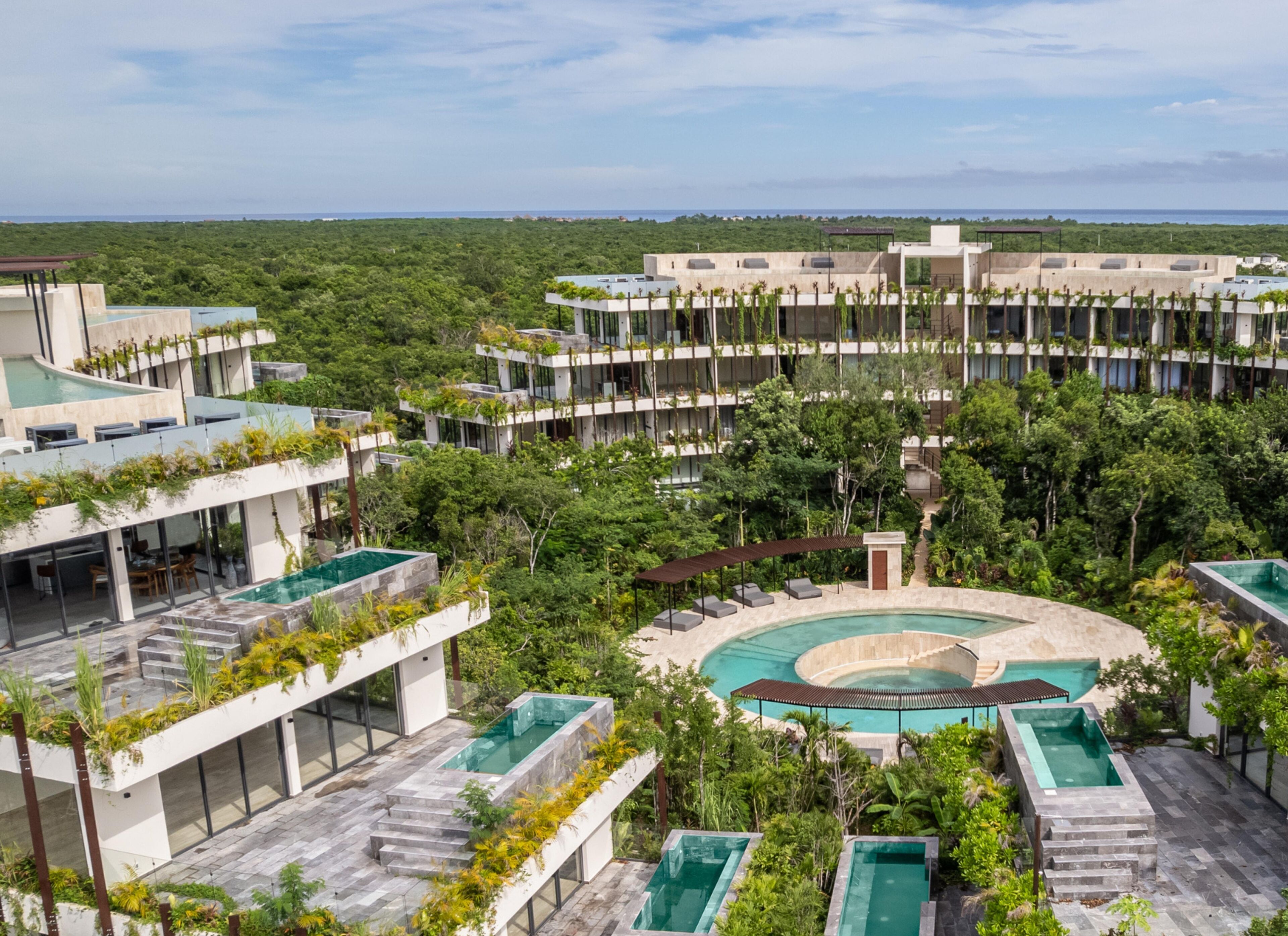Ein modernes Hotel mit mehreren Schwimmbecken, üppiger Vegetation und Blick auf den Ozean.