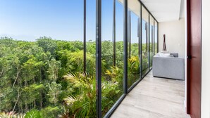 A balcony with a view of a dense forest, a grey sofa, and a wooden floor. - Mistiq Temple II  (Tulum)