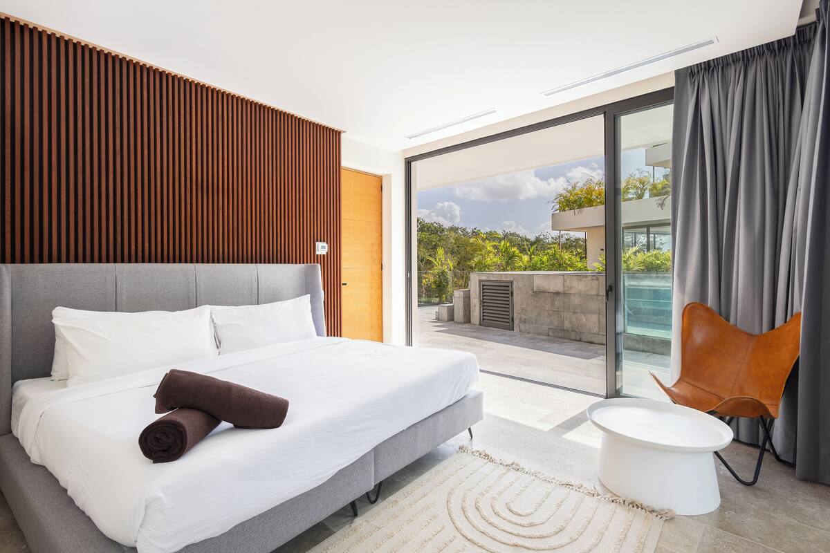 A modern hotel room with a large bed, a small round table, and a view of the outdoors.