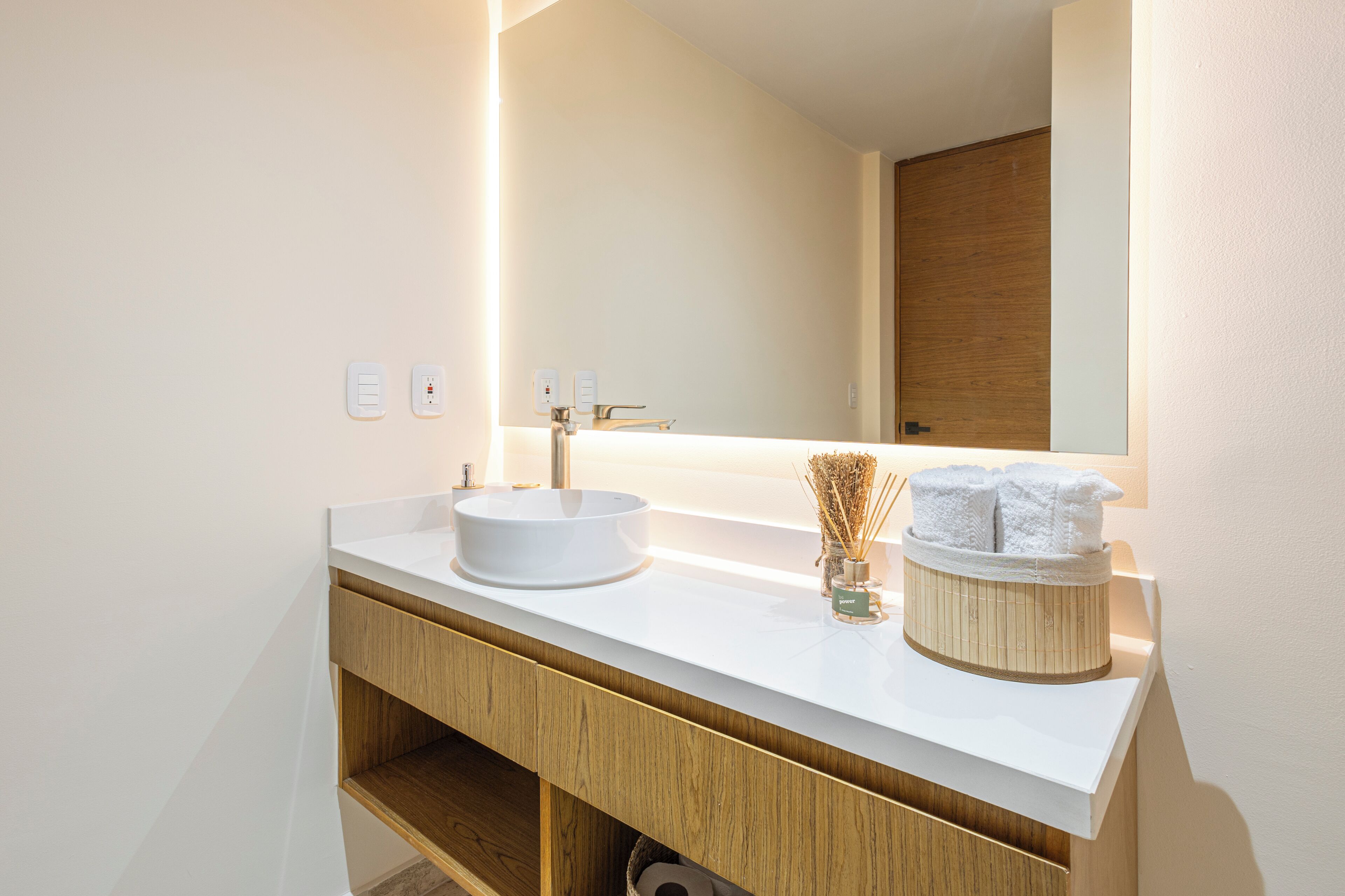 Un bagno moderno con un lavandino bianco, un mobile bagno in legno e uno specchio sopra il lavandino.