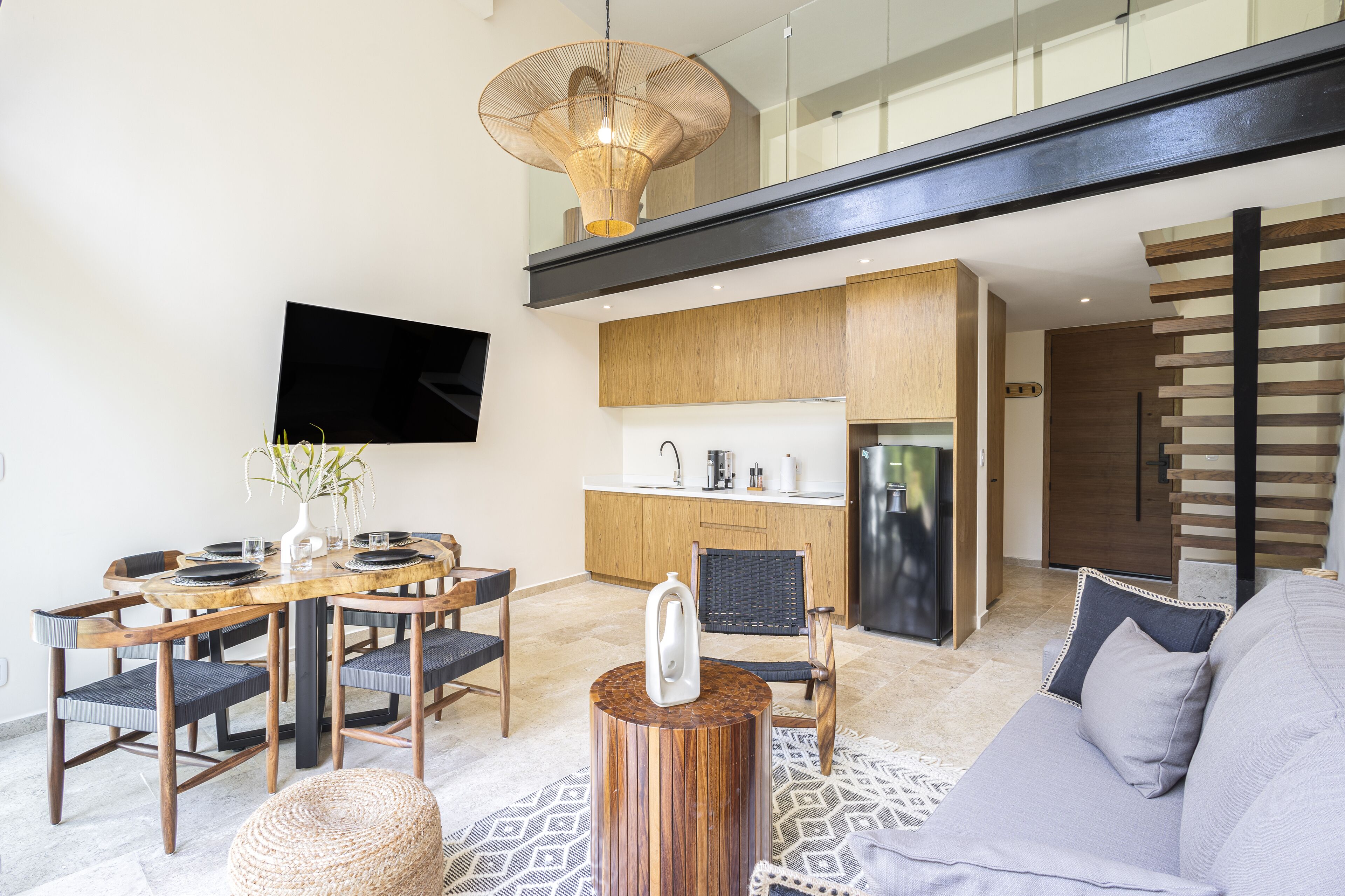 A modern living room with a dining area, a kitchen, and a staircase.