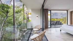 A modern balcony with glass railings, wicker furniture, and a view of the surrounding greenery. - Mistiq Temple II  (Tulum)