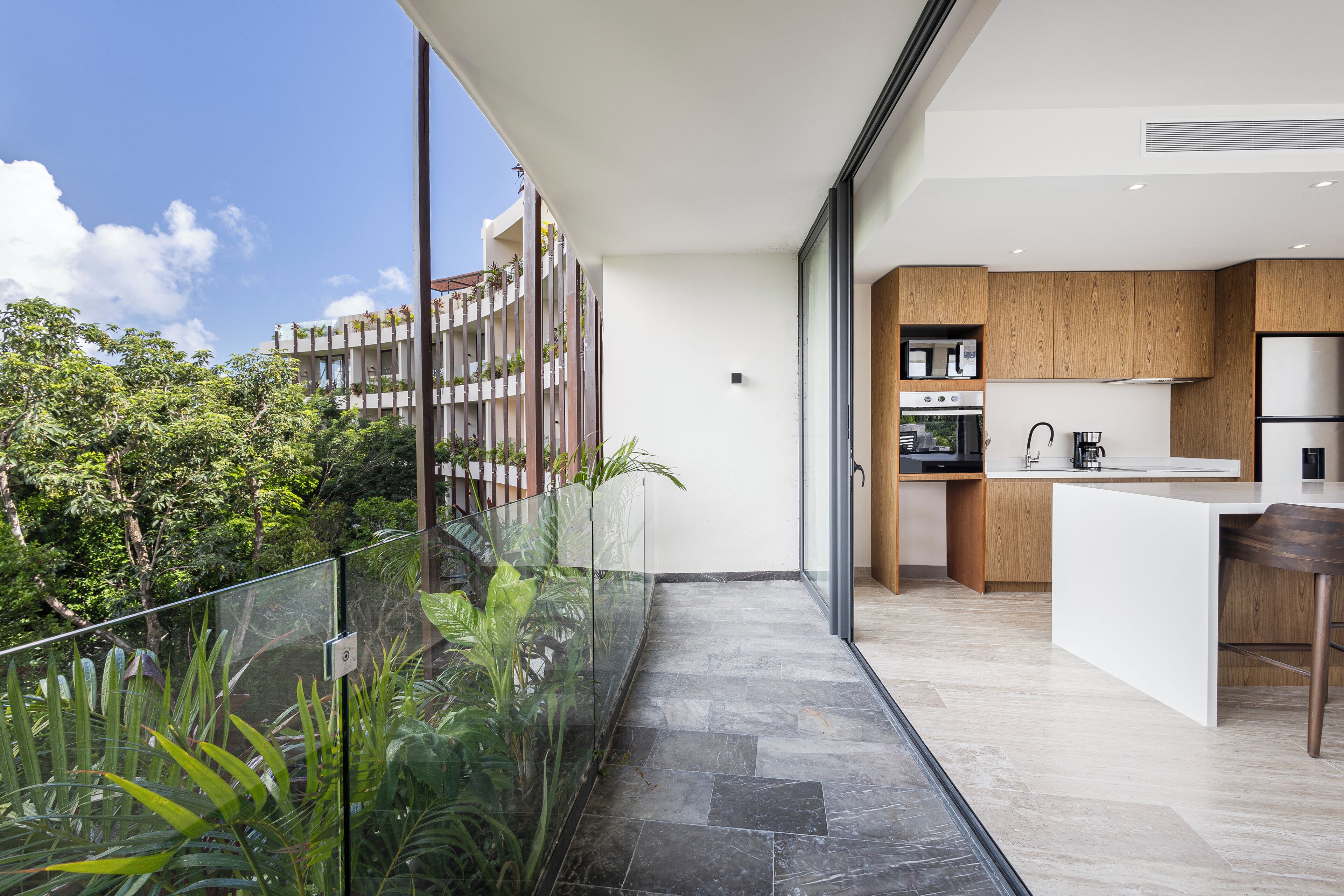 A modern kitchen with a large island, built-in appliances, and a glass railing overlooking a lush garden.