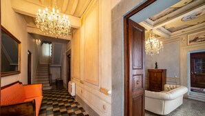 A grand hallway with a checkered floor, a wooden bench, a door, and a chandelier.