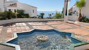 Ein Swimmingpool mit einer runden Steinanordnung in der Mitte, umgeben von einer weißen Mauer und einer gefliesten Terrasse.